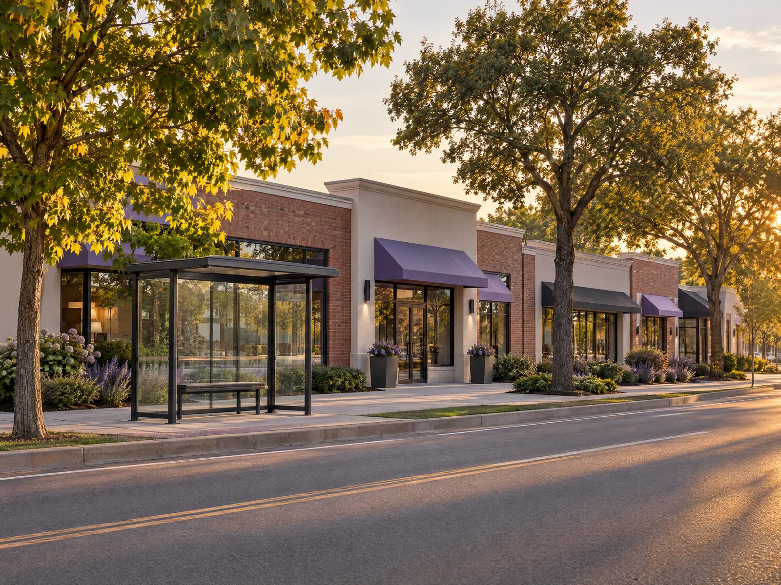 Single story shopping plaza with lavender awnings and a glass bus shelter at golden hour